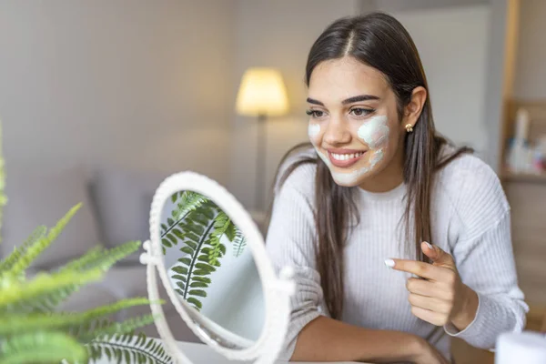 年轻快乐的女人做面部按摩用有机洗脸和镜子在家里 女孩使用洗涤剂 剥皮和清洁皮肤 迷人的女孩 戴着保湿的面膜 — 图库照片