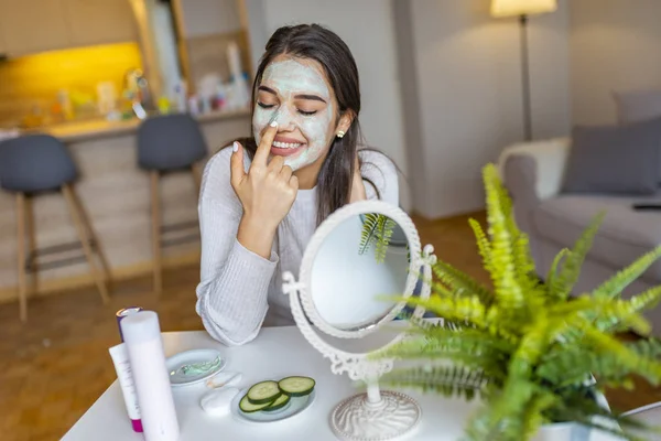 So beautiful. Close-up of girl with beauty mask on her face looking in mirror. Girl uses natural mask. Attractive young woman sitting with a facial mask on her skin
