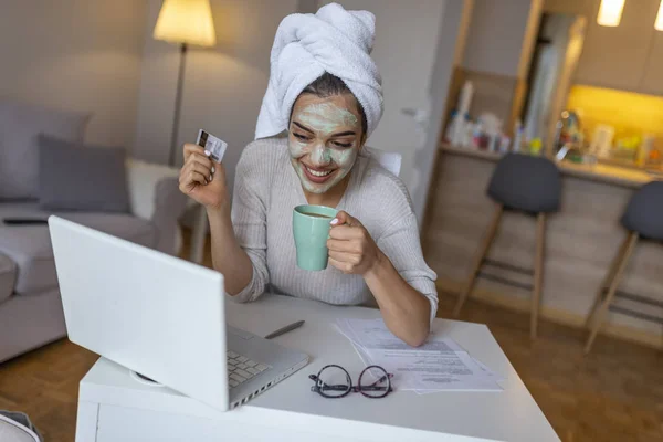 Woman with cosmetic face mask shopping online from her home. Close Up of Woman with Clay Mask on Her Face, Using laptop for Shopping Online .