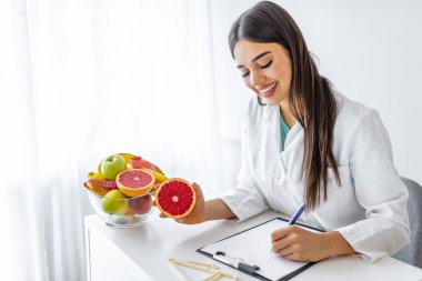 Ofisinde gülümseyen beslenme uzmanı, sağlıklı sebzeler ve meyveler, sağlık hizmetleri ve diyet konsepti gösteriyor. Masasında meyveleri olan kadın beslenme uzmanı.. 