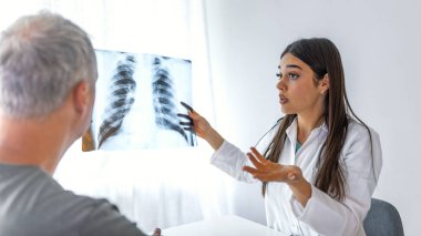 Kadın doktor, hastasına röntgen görüntüsü kullanarak check-up sonuçlarını açıklıyor. Klinikte oturan hastaya röntgen görüntüsü teşhisi koyan tıp uzmanı..