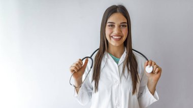 Neşeli doktor. Beyaz üniformalı neşeli bayan doktor gri arka planda dururken gülümsüyor. Dost canlısı, mutlu, genç bir hemşire ya da boynunda steteskop olan bir doktor.