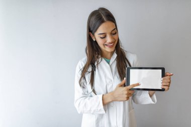 Beyaz önlüklü gülümseyen genç doktorun portresi elinde dijital tablet ekranını gösteriyor. Ekran için kırpma yolu ile beyaz arkaplan üzerinde boş dijital tablet tutan doktor