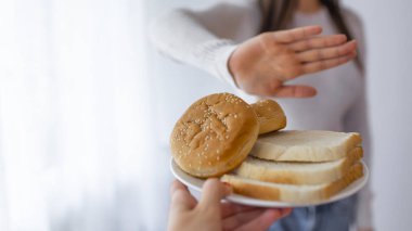 Young woman on gluten free diet is saying no thanks to toast. A woman on a gluten free diet is saying no thanks to toast. Woman refusing to eat white bread clipart