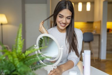 Genç bir esmer kozmetik güzelinin portresi. Aynaya bakan mutlu genç bir kadın. Yuvarlak aynada yüzünü inceleyen bir kadın. Kadın yüz derisine nemlendirici sürüyor.