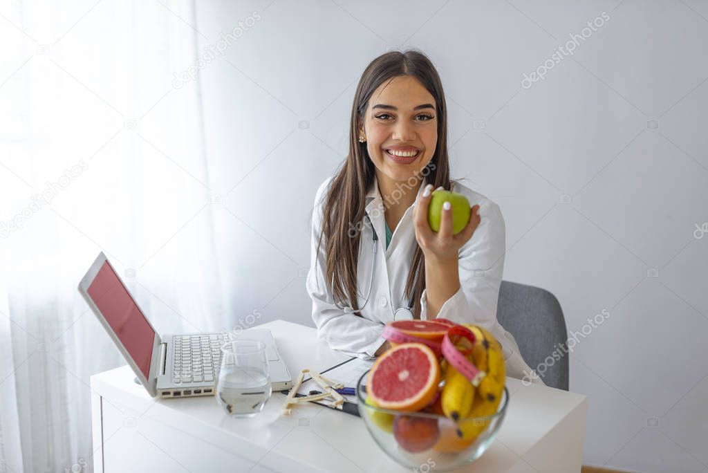 Nutritionist desk with healthy fruits, juice and measuring tape. Dietitian working on diet plan at office, smiling at camera. Weight loss and right nutrition concept. 