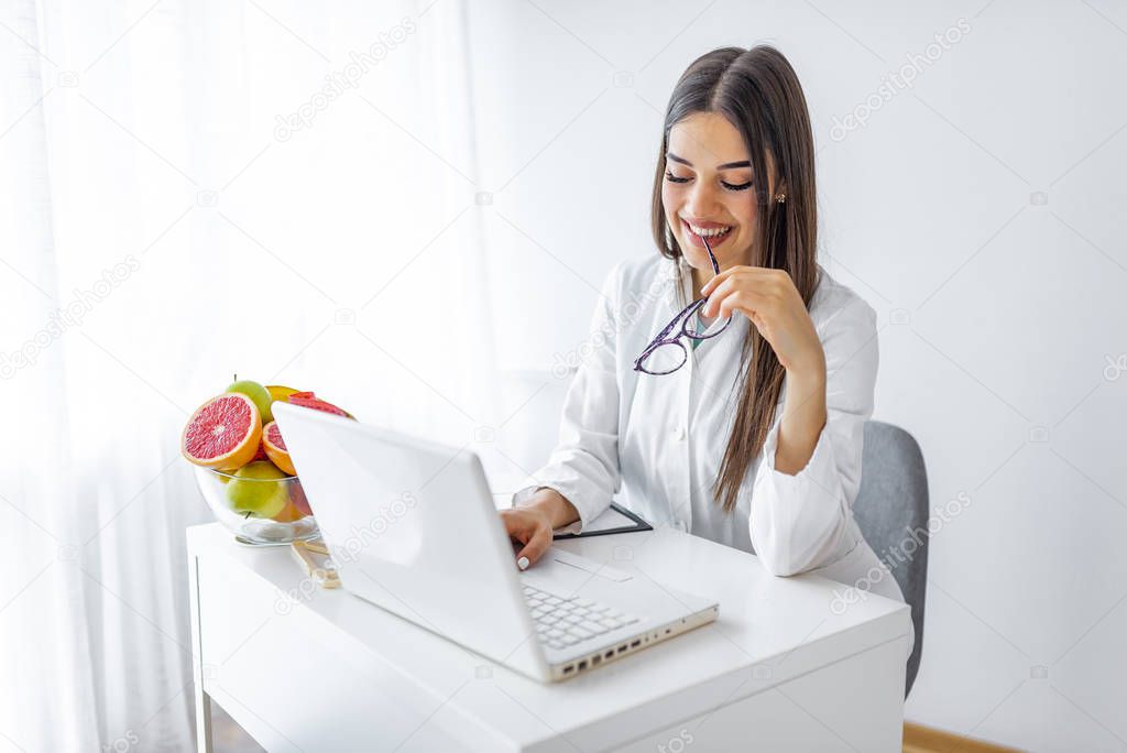 Nutritionist desk with healthy fruits, juice and measuring tape. Dietitian working on diet plan. Weight loss and right nutrition concept. Female nutritionist sitting at table with clipboard and healthy products