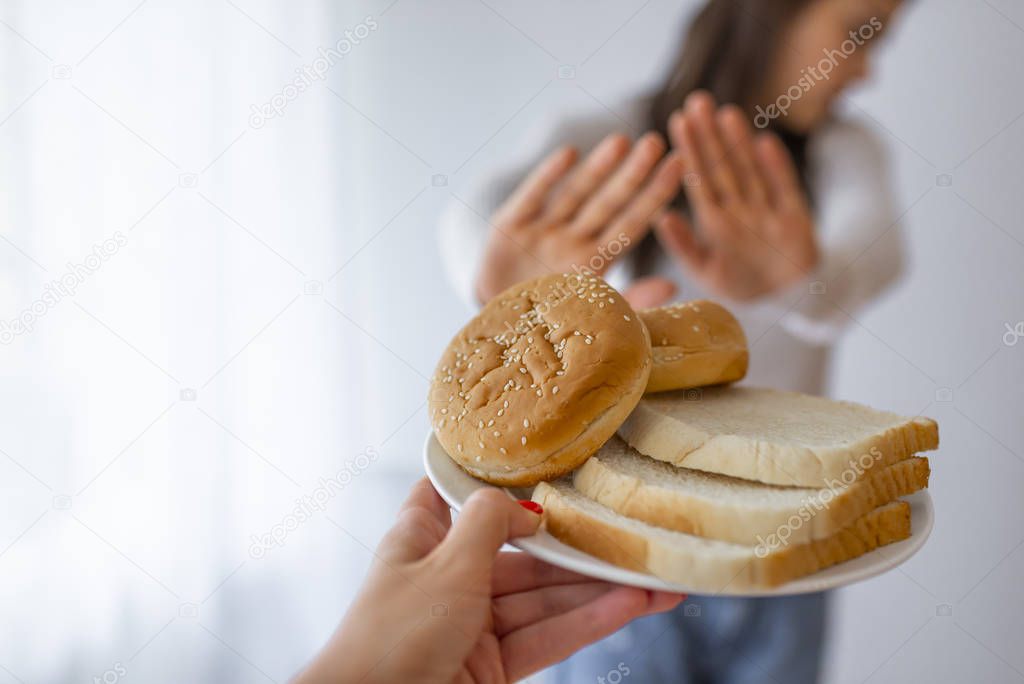 Young woman suffers from a gluten. Gluten intolerant and Gluten free diet concept, Real people. Copy space. Gluten intolerance and diet concept. Woman refuses to eat white bread. Selective focus on bread