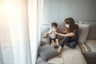 Anne ve çocuk koronavirüs ve grip salgını sırasında yüz maskesi takıyor. Virüs ve hastalık koruması. Annem küçük oğluna tıbbi maske takıyor. Anne ve oğul hastalıkların yayılmasını engellemeye çalışıyor.