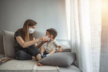 Anne ve çocuk koronavirüs ve grip salgını sırasında yüz maskesi takıyor. Virüs ve hastalık koruması. Annem küçük oğluna tıbbi maske takıyor. Anne ve oğul hastalıkların yayılmasını engellemeye çalışıyor.
