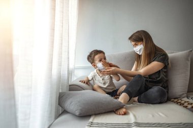 Anne ve oğlu maske takıyor ve kendilerini Covid-19 'dan koruyorlar. Anne çocuğuna koruyucu yüz maskesi takıyor. Yüzü maskeli anne ve çocuk. 
