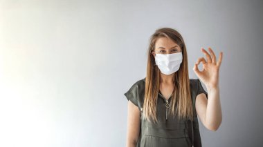 Tıbbi maske takan genç bir kadın, stüdyo resmi. Koruyucu maske takan ve onay işareti gösteren bir kadın. Corona virüsü için ameliyat maskesi takan kadın.. 