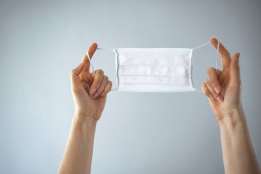 Gri arka planda tıbbi koruyucu maske tutan kadın eller. COVID19 'a karşı çevre ve virüs koruma kavramı. Tıbbi maske elinde.