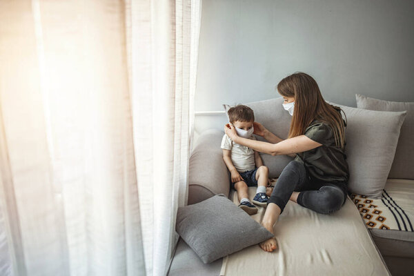 Боковой вид взрослой женщины, надевающей медицинскую маску на маленького мальчика во время вспышки коронавируса на сером фоне. Мать и ее сын надевают маски, защищая себя от вирусов
