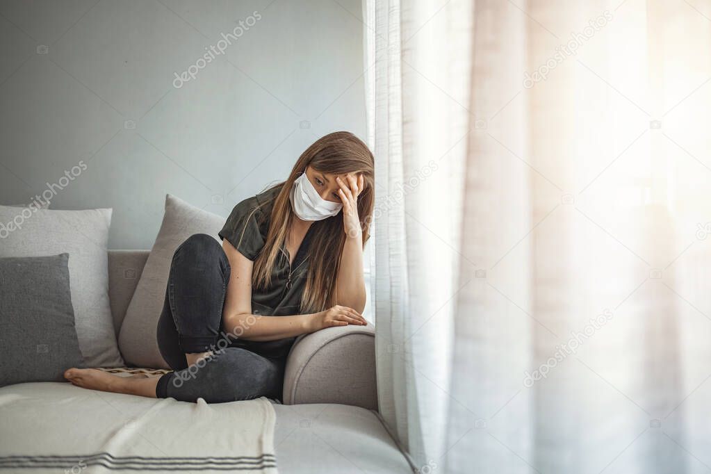 Sad lonely girl isolated stay at home in protective sterile medical mask on face looking at window, bored woman because of Chinese pandemic coronavirus virus covid-19. Quarantine, prevent infection