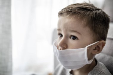 Coronavirus Covid-19 'a karşı önlem olarak solunum maskesi takan küçük bir çocuk. Anti virüs maskesi takan küçük çocuk evde kalıyor. Grip ve virüs enfeksiyonuna karşı koruma