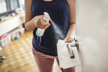 Kadın dezenfeksiyon spreyi ve tek kullanımlık mendille kapı kolunu temizliyor. Kadın antibakteriyel spreyle kapı kolunu sterilize ediyor. Coronavirüs salgını sırasında evde kalan kız