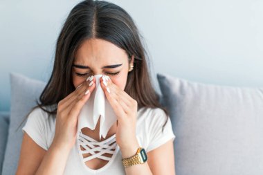 Konsept koronavirüs, solunum virüsü. Ağrının yerini gösteriyor. Sağlık sigortası, soğuk, alerji ve evdeki kağıt mendile akan burnunu silen hasta kadın.