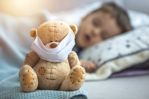 彼の病気のテディベアの医療マスクで ベッドでの家庭の隔離での子供は コロナウイルスCovid 19とインフルエンザの流行の間のウイルスに対する保護のために 寝ています 子供と病気の概念 — ストック写真
