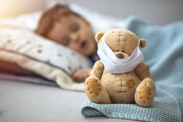 テディベアとベッドで寝ている男の子は コロナウイルスから彼を守るためにマスクをしていますCovid 2019 Nconvの概念 愛らしいです幼児男の子取りますA昼寝でAホワイトベッド保持彼のテディベア — ストック写真