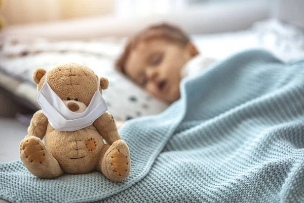 Маленький Хлопчик Спить Ліжку Медичною Маскою Обіймаючи Свого Плюшевого Ведмедя — стокове фото
