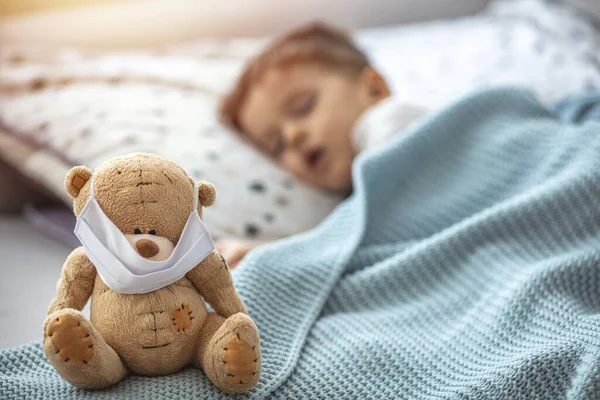 Portrait of a little kid sleeping and teddy bear using air masks. Child in home quarantine sleeping. Medical mask on his sick teddy bear, for protection against viruses during coronavirus COVID-19 and flu outbreak