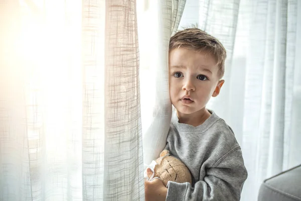 Child in home quarantine. Boy sits on windowsill and looks out window, sitting home, wants to walk. Virus protection, coronavirus pandemic, prevention epidemic. Stay at home quarantine for coronavirus pandemic prevention.