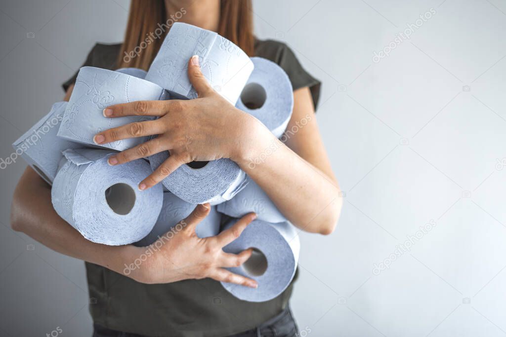 Close up shot adult woman try to keep balance while holding large group of toilet paper with both of her hands, amidst Covid 19 panic buying. Woman grabbing rolls of toilet paper. Covid-19 panic outbreak 