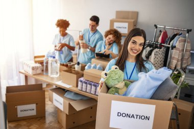 Small group of people working on humanitarian aid project. Cheerful food drive manager. Confident woman volunteers as a manager of a food and clothing drive in her community or church clipart