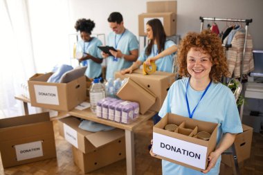 Small group of people working on humanitarian aid project. Cheerful food drive manager. Confident woman volunteers as a manager of a food and clothing drive in her community or church clipart