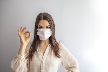 Coronavirus salgını: Bulaşıcı virüslerden kaçınmak için tıbbi tek kullanımlık maskeli bir kadın, tamam işareti gösteriyor. Corona virüsünün önlenmesi. Koronavirüs karantinası kavramı. Dikkat! 