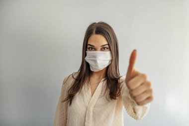 Yüz koruyucu maskeli bir kadın gri duvarın önünde duruyor, salgın hastalıklardan korunuyor, solunum enfeksiyonlarından korunuyor, parmağını gösteren bir kadın var. Viral zatürree, grip, MERS-CoV, SARS için kavramsal görüntü