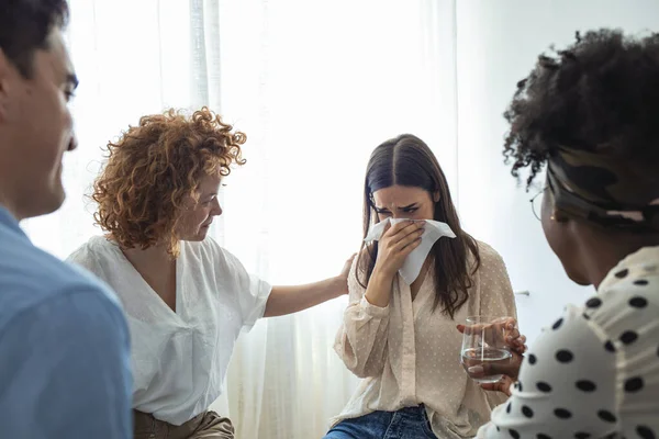 Multi-ethnic group of people in counseling session with therapist. Therapy crisis. Depressed woman crying at support meeting, therapist comforting her. Rehab group at therapy session