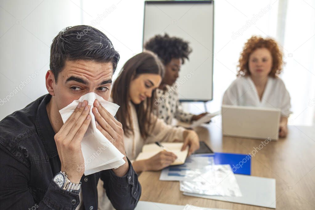 Cropped shot of a businessman suffering with allergies in an office. Shot of a frustrated businessman using a tissue to sneeze in while being seated in the office. Working when sick