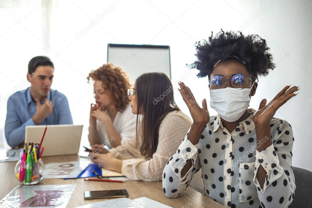 Serious businesswoman in protective mask looking at the camera in his office and people in background. Employee working in business office while wearing medical face mask