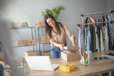 İnternette ürün satan ve nakliye için paket yapan genç bir kadın. Kadınlar, küçük işletmelerin sahibi kutular içinde ürünleri paketleyip teslimat için hazırlıyorlar.