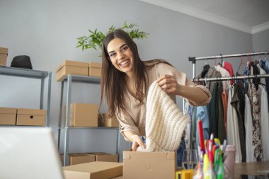 İnternette ürün satan ve nakliye için paket yapan genç bir kadın. Kadınlar, küçük işletmelerin sahibi kutular içinde ürünleri paketleyip teslimat için hazırlıyorlar.