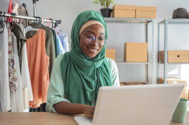 Müslüman bir kadın kendi evinde küçük bir iş yürütüyor. Giysilerin tasarımı ve terziliği. İş raporları ve hesap makinesiyle finans hakkında çalışan güzel Müslüman kadın.