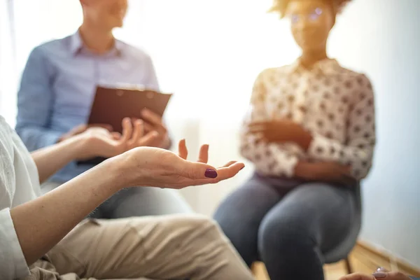 Close-up of a therapist gesticulating while talking to a group of listing teenagers during an educational self-acceptance and motivation meeting. People at group psychotherapy session indoors