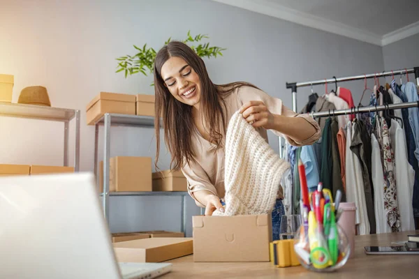 Young woman selling products online and packaging goods for shipping. Women, owener of small business packing product in boxes, preparing it for delivery