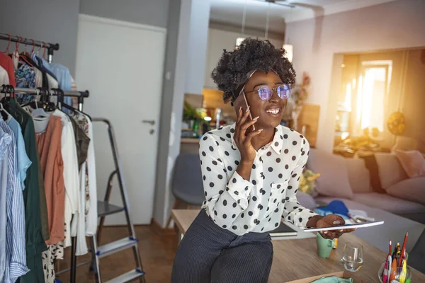 アフリカ系アメリカ人のビジネスマン自宅のオフィスで電話でタブレットPcを持つ女性 彼女の机に座っている間に電話で話して魅力的な若い女性のショット — ストック写真
