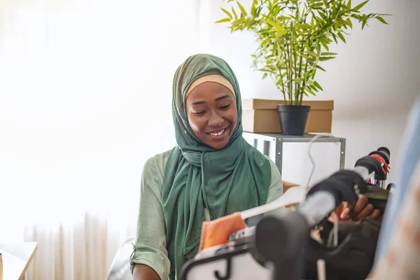 テーラーショップで働くスタートアップビジネスオーナーとしてのムスリム女性デザイナー 小規模事業主 ワークショップで働く美しい若いアフリカ人女性 オンラインショッピングは多くの人々を幸せにします — ストック写真
