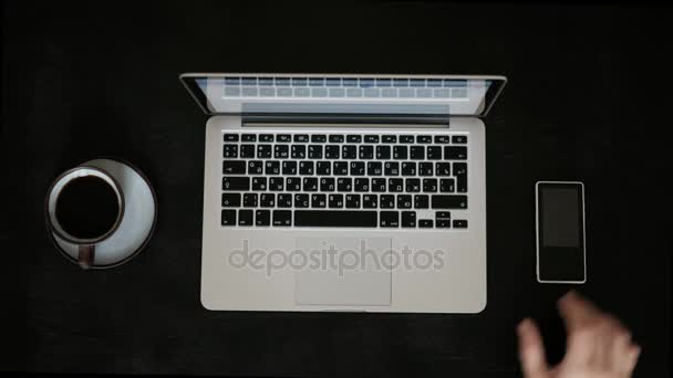 Bir fincan kahve ile bir dizüstü bilgisayar üzerinde çalışan bir erkeğin doğrudan siyah masa — Stok video