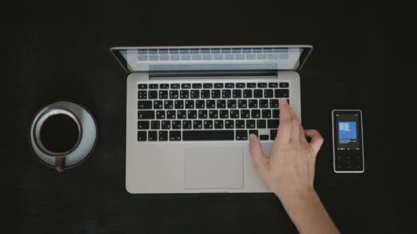 Прямо над черным столом человек, работающий над ноутбуком с чашкой кофе — стоковое видео