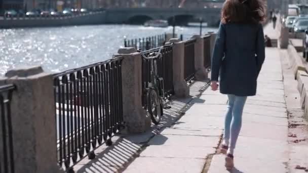 Chica joven y feliz con el pelo largo, chaqueta de mezclilla, corriendo por la calle y escuchando música en los auriculares — Vídeos de Stock