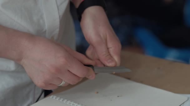 Close-Up: El hombre afilando el lápiz negro del cuchillo, en el fondo del libro de texto — Vídeo de stock