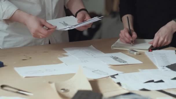 Dva módní návrháři ve studiu, nakreslit náčrtek oblečení, v černé a bílé trička, nakreslete tužkou v poznámkovém bloku — Stock video