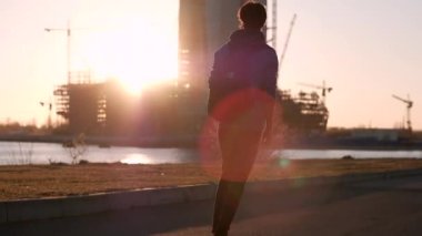 Genç adam bir kaykay üzerinde arka plan yapım aşamasında, bir gökdelenin üzerinde günbatımında geri görünüm alma