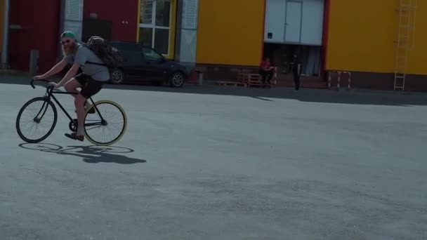 Le barbu chevauche le vélo vintage noir en été, en short noir, une casquette verte, lunettes, sac à dos — Video