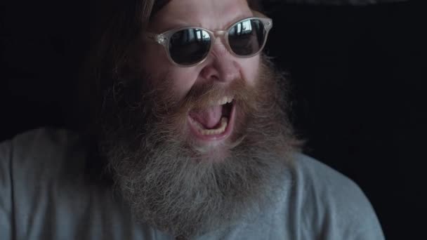 Portret van een agressieve bebaarde Man in glazen op een zwarte achtergrond, de Man Grins, mond, tanden waaruit openen — Stockvideo